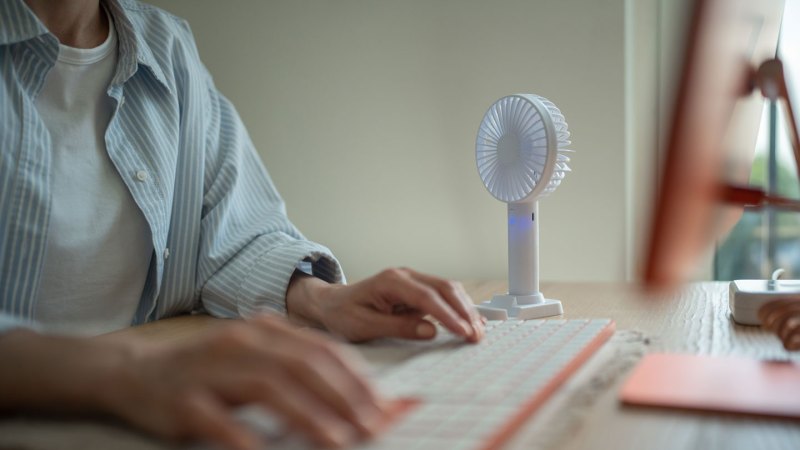 A person types on a keyboard next to a small fan